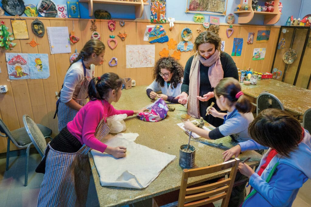 A woman observes children making crafts in a classroom.
