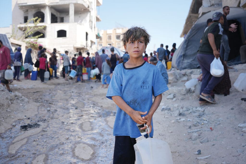 A boy with an empty jug standing on a street.