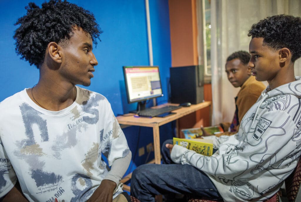 Three young men look around a computer.