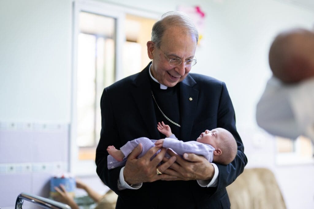 Archbishop Lori holds an infant at the Crèche in Bethlehem, Palestinian West Bank.