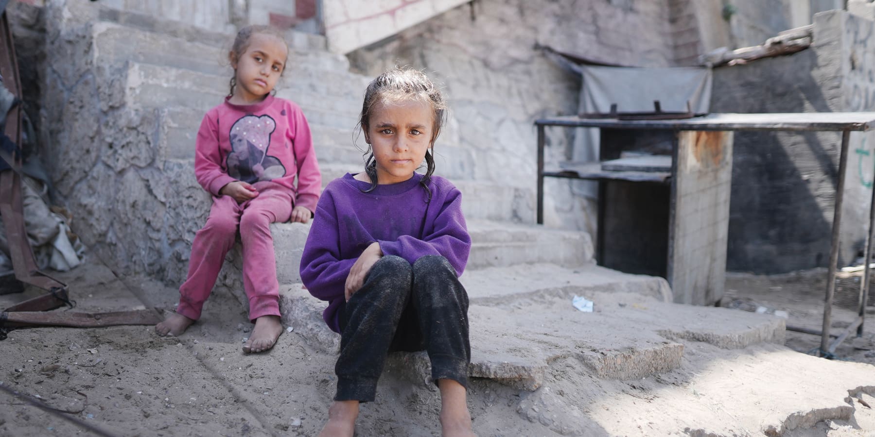 Two little girls sitting on the steps of a destroyed building.