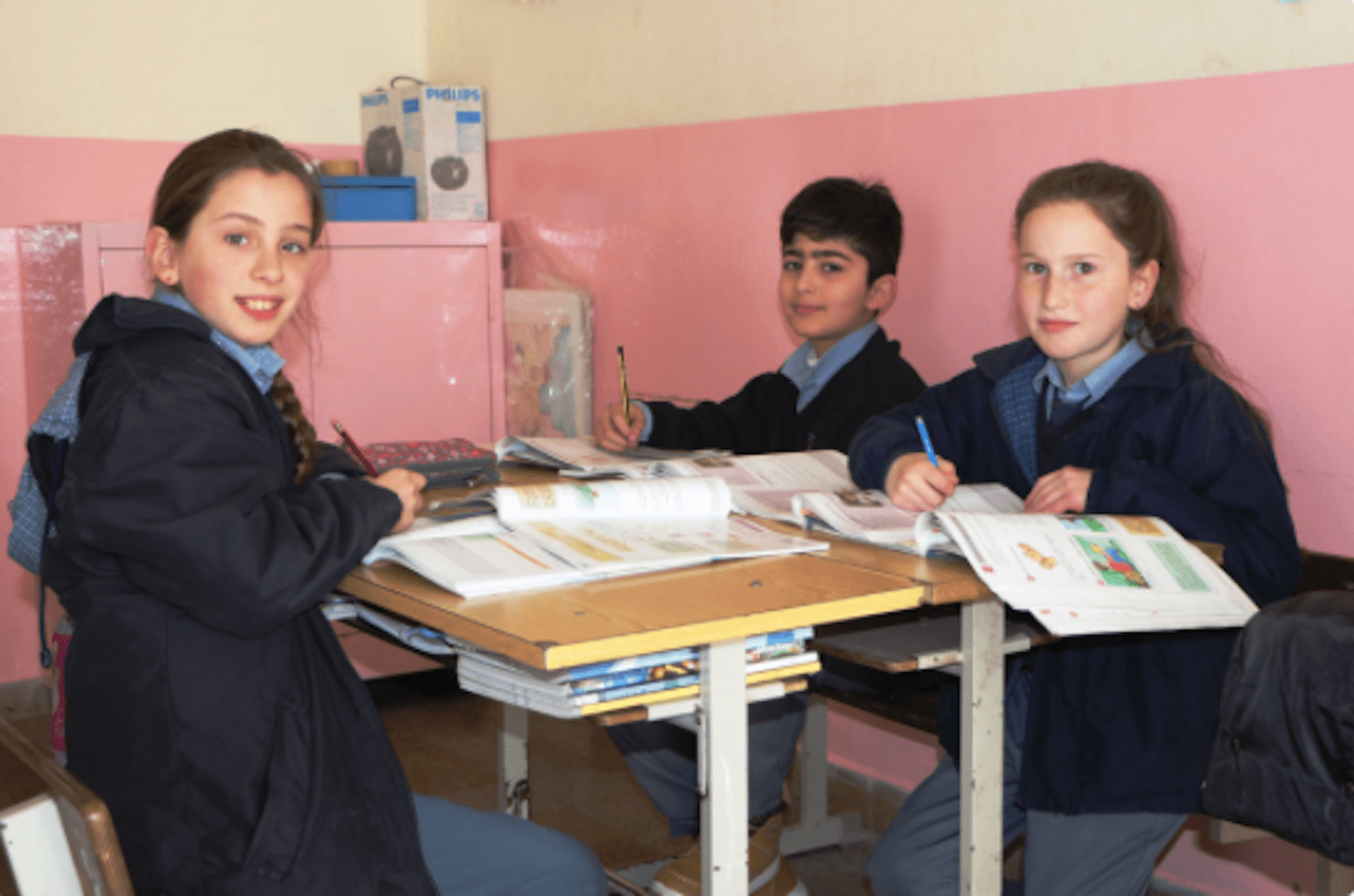 Three school children sitting at a desk.