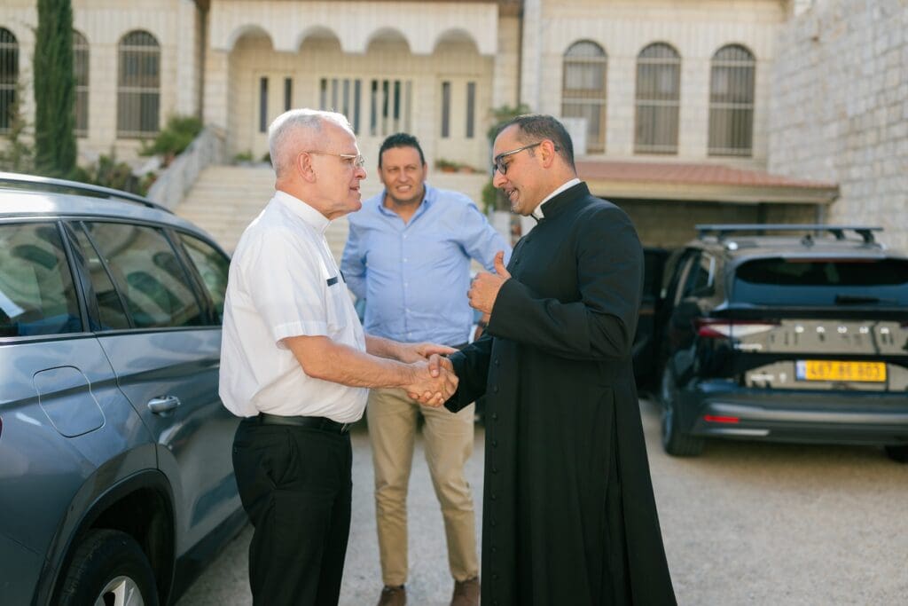 Two priests shake hands while another man observes.