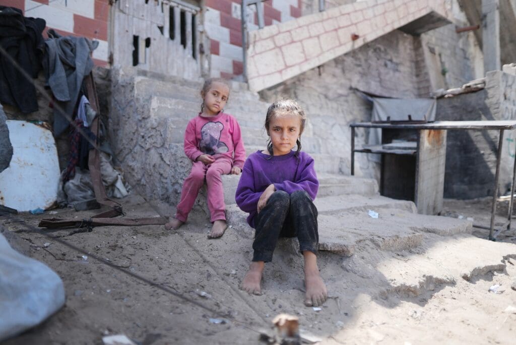 Two little girls sitting on the steps of a destroyed building.