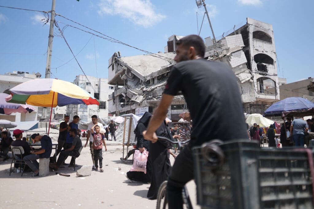 Man on bycicle rides through a market near a destroyed building.