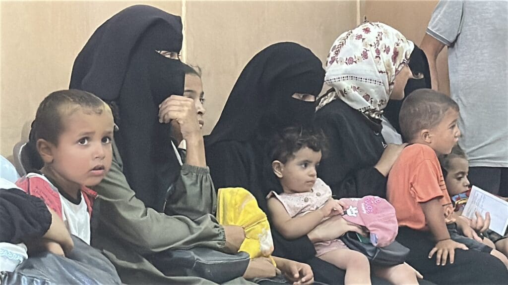 Four mothers wearing hijabs are seated carrying their children.