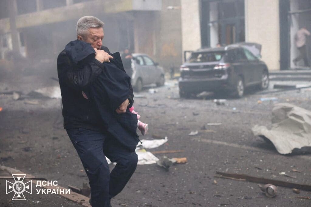 A man evacuates a child from the kindergarten hit by a Russian drone strike.