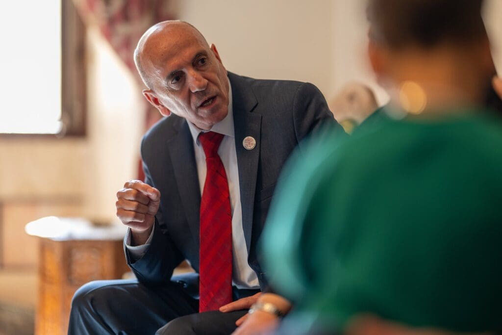Joseph Hazboun, in a suit, is seated whole talking to another person.