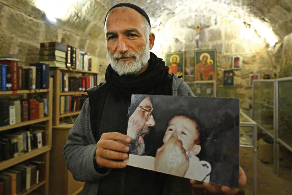 Father Jihad Youssef holds an image of Father Paolo Dall’Oglio holding a baby.