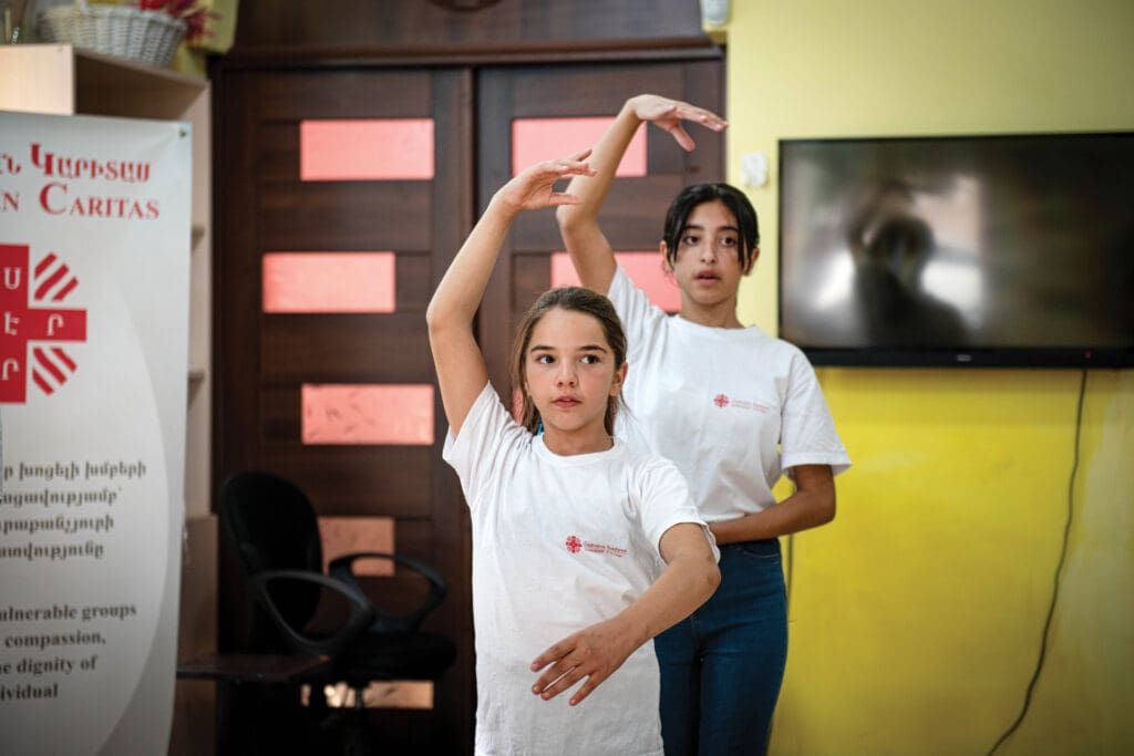 Two girls wearing Caritas T-shirts are dancing.