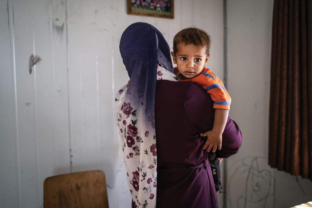 Seen is the back of a woman wearing a hijab and carrying a child.