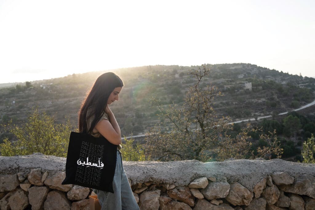 A woman walks, in the background a knoll in the West Bank.