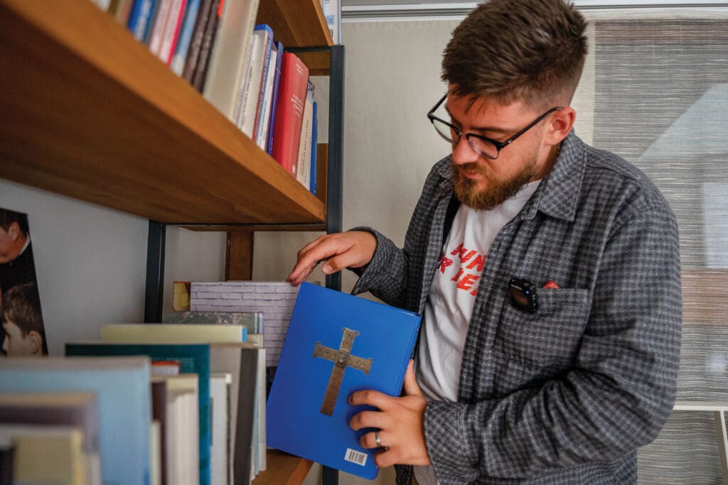 A man pulls a book with a cross on the cover from a bookshelf.