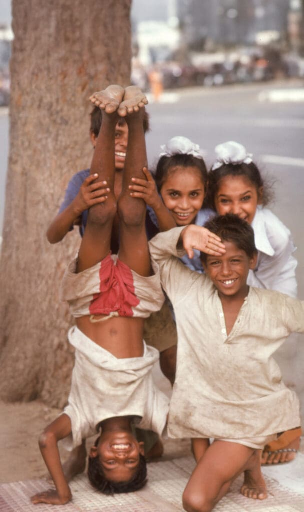 Five children smile to the camera, one of them is standing on his head.