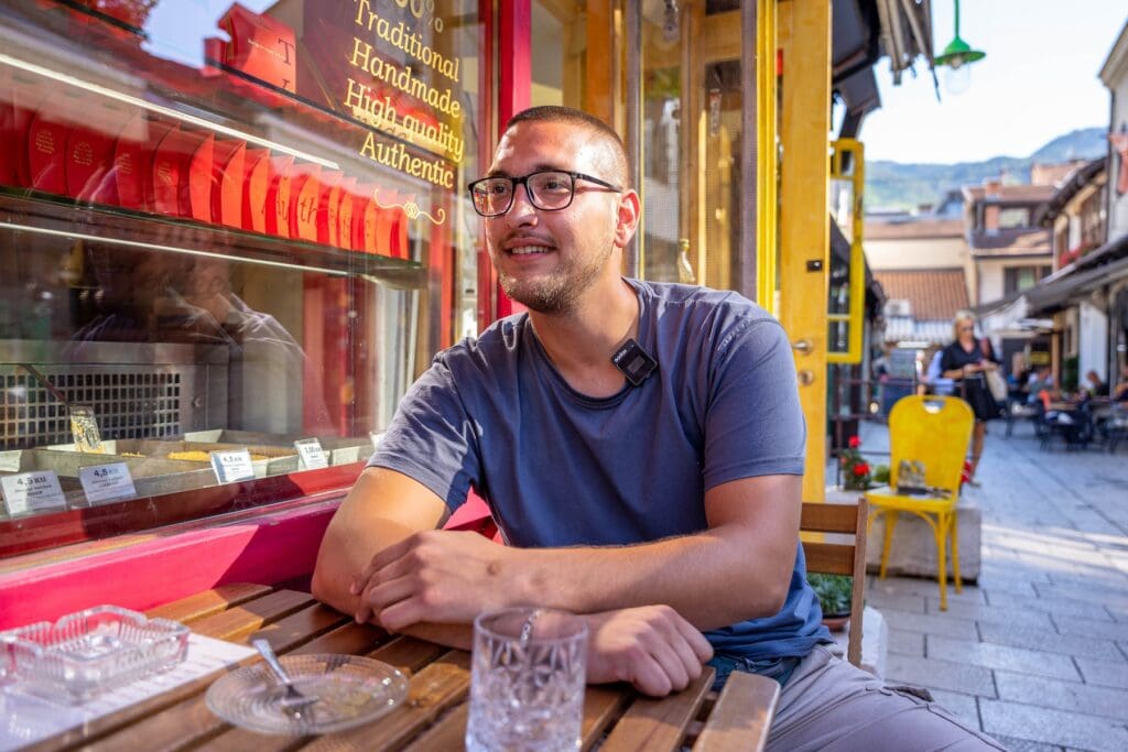 Man waring glasses sits outside a coffee shop.