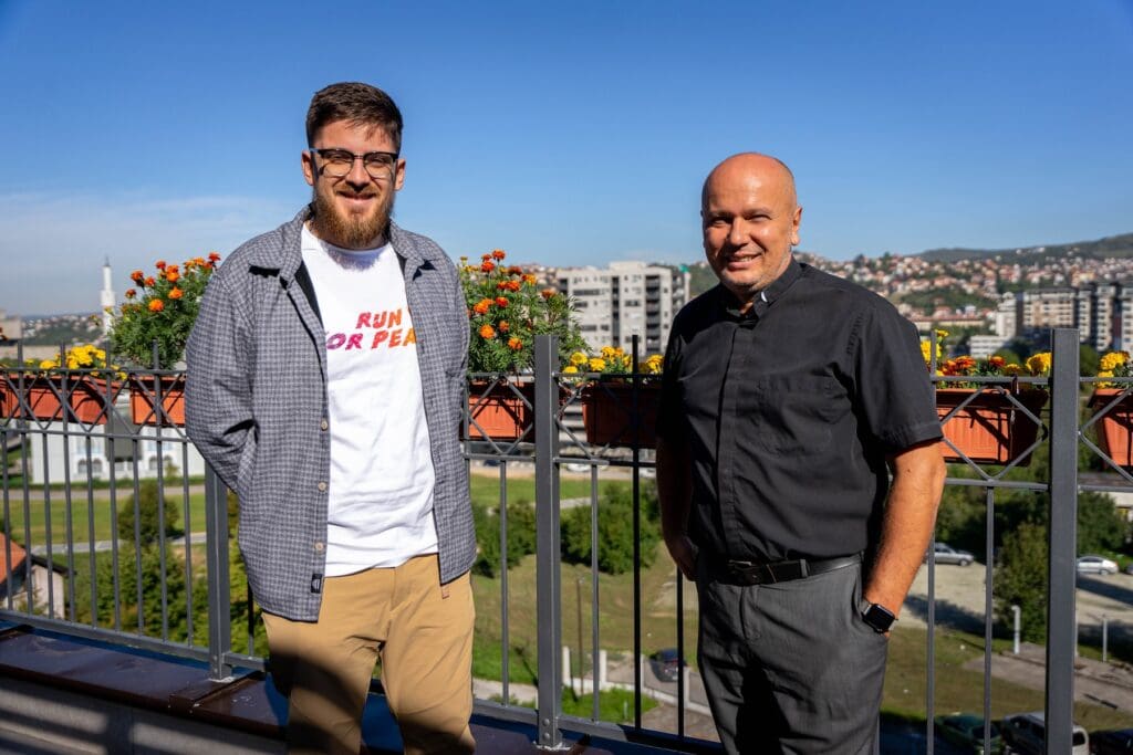 A man and a priest smiling at the camera.