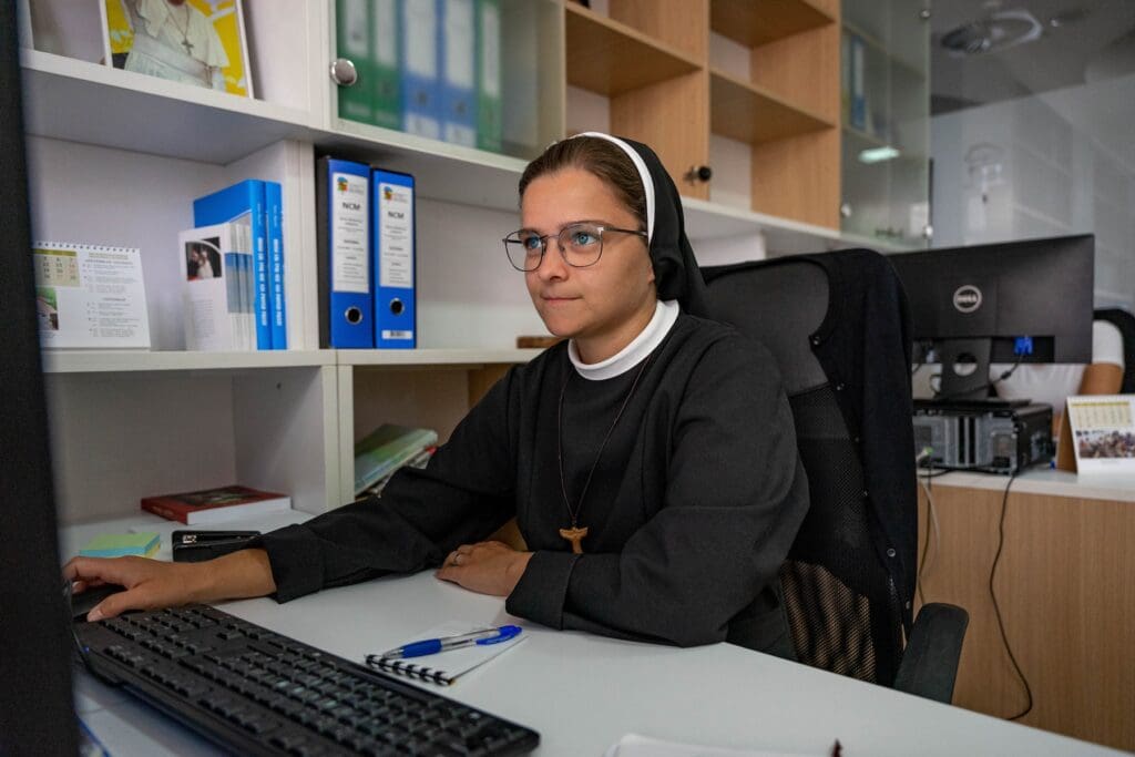 A young religious sister sitting at a desk and using a computer.