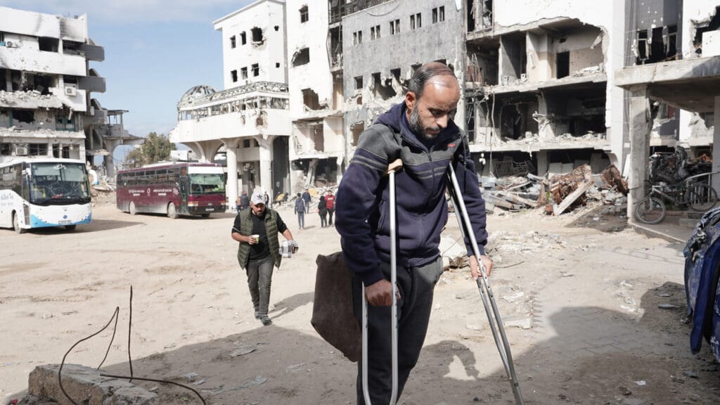 A man in crutches passes by mostly destroyed buildings in Gaza City.