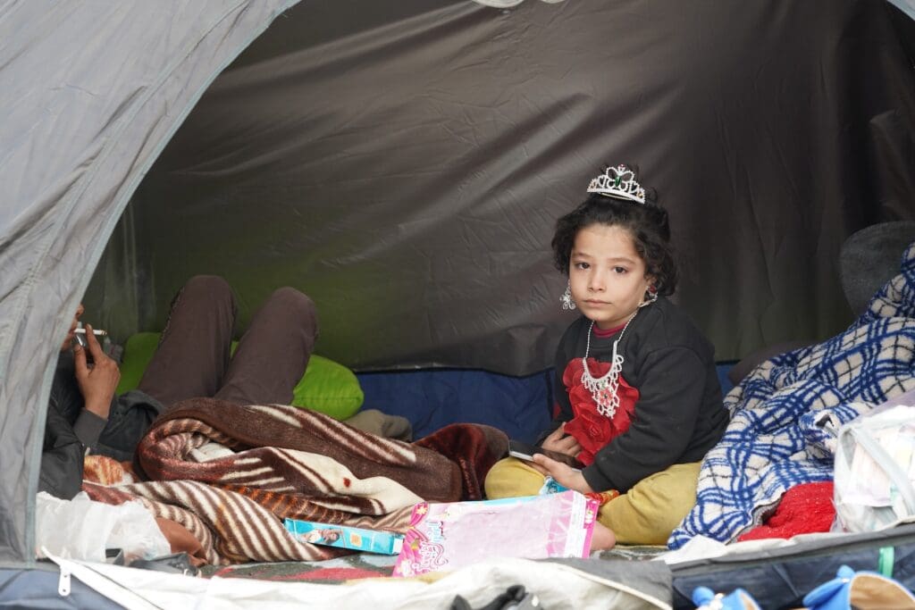 A little girl wearing a crown sits in a tent for refugees.