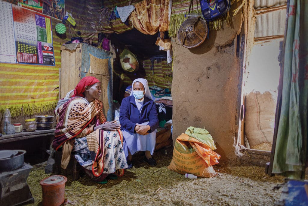 A religious site wearing a mask sits next to an Ethiopian woman in a small hut.