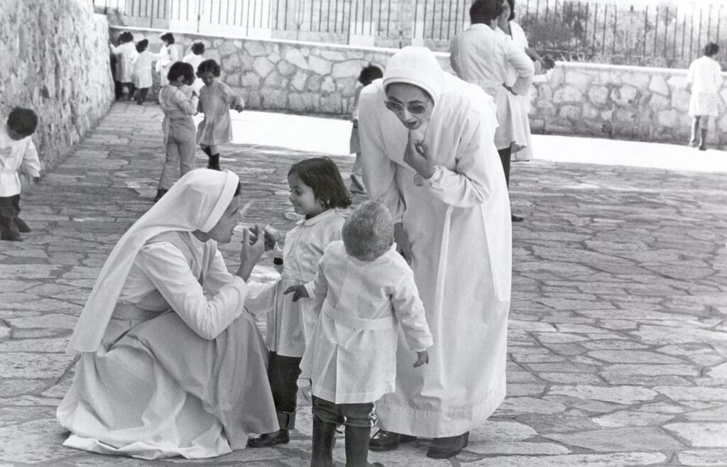 two religious sisters play with children at a school yard.