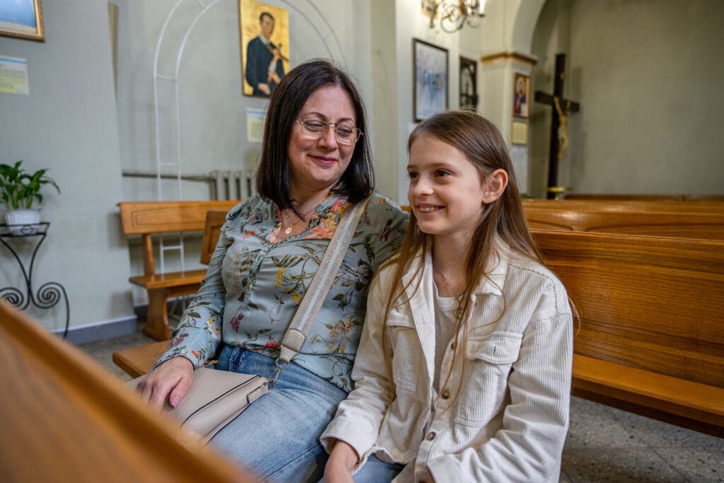 A woman and her daughter sitting on a pew in a church.